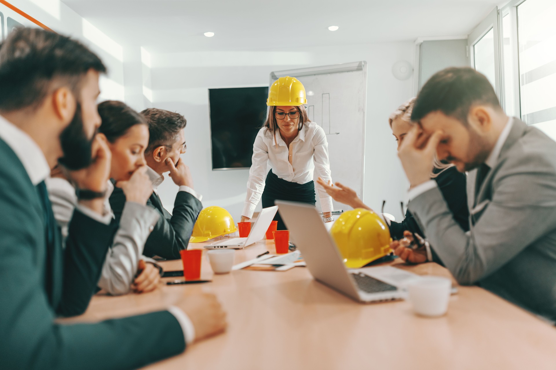 Smiling female boss in formal wear and with protective helmet on head leaning on desk and talking about project. Architect business concept. Tough times don't last, tough times do.